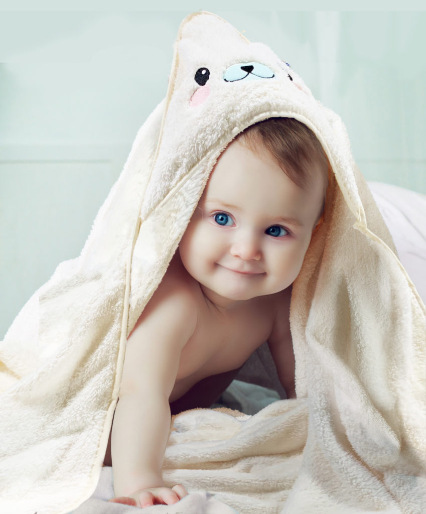 six months old baby with a towel after taking a bath, in bed at home